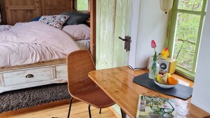 A rustic room with a bed, a dining table with chairs, a cowhide rug, and a window with a view of greenery.
