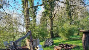 A rustic outdoor setting with a wooden structure, a stone bench, and a pile of firewood.