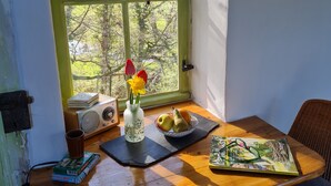 A wooden table with a bowl of fruit, a vase with flowers, a book, and a cup.