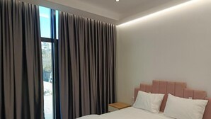 A bedroom with a bed, curtains, a nightstand, and a window. - Rezidenca Pahumi 2 (Durrës)