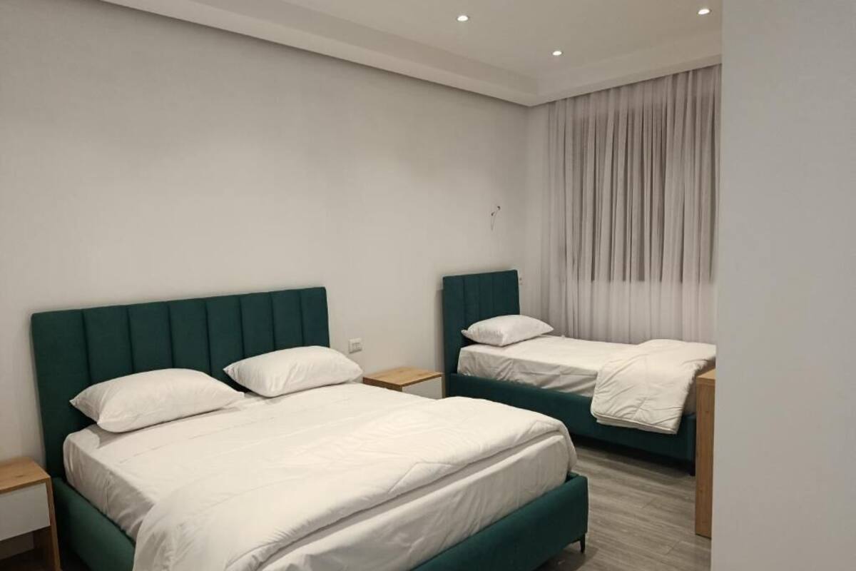 A hotel room with two beds, a wooden nightstand, and a window with curtains.