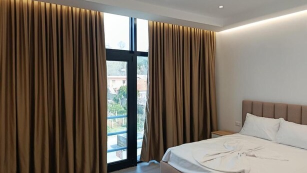 A hotel room with a bed, curtains, and a view through a large window. - Rezidenca Pahumi 2 (Durrës)