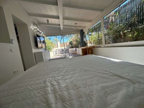 Quarto com cama grande, TV fixada na parede e vista para o exterior através de amplas janelas.