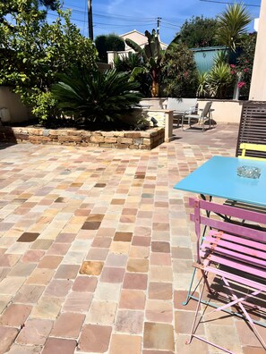 Um pátio com ladrilhos de pedra, uma mesa azul e um banco rosa.