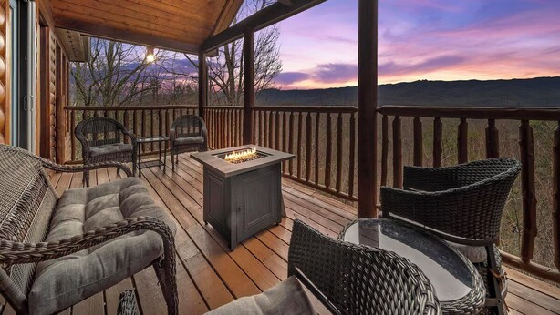 Une terrasse en bois, meublée de meubles en osier, avec un foyer et une vue sur le paysage.