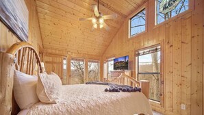 Une chambre dans une cabane en bois, avec un lit, un ventilateur de plafond et un téléviseur.