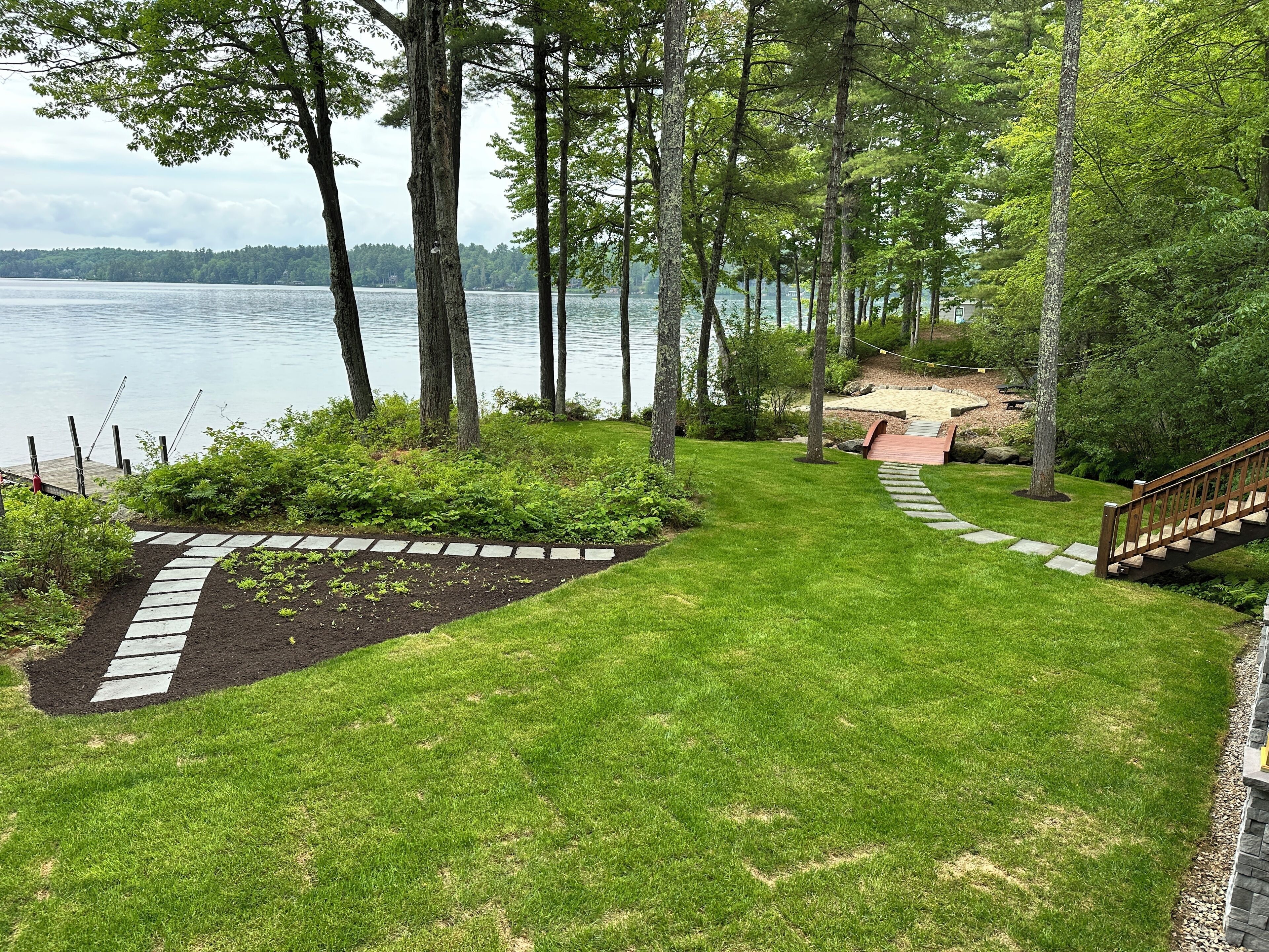 A well-maintained garden with a stone pathway leading to a wooden deck overlooking a lake.