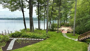 Un jardín cuidado con un sendero de piedra que conduce a una terraza de madera con vista al lago.