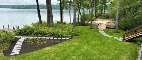 A well-maintained garden with a stone pathway leading to a wooden deck overlooking a lake.