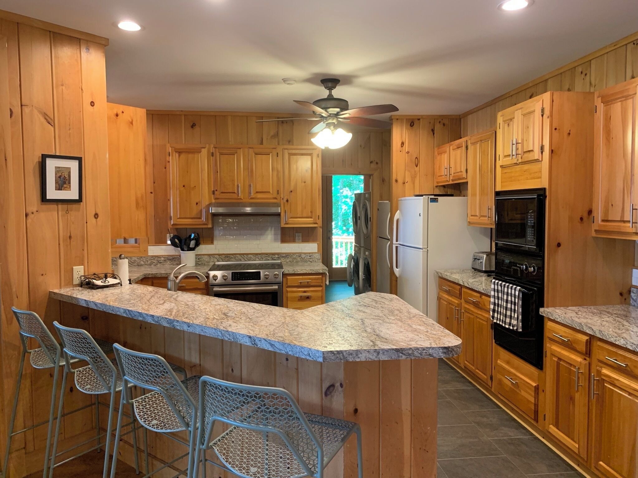 A kitchen with wooden cabinets, a granite countertop, a ceiling fan, and a built-in oven.