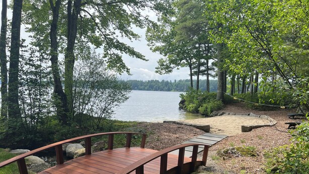 Una terraza de madera con barandilla curva que da a un lago, rodeada de árboles y rocas.