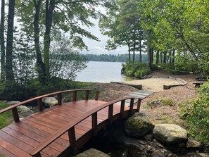 Um deck de madeira com guarda-corpo curvo, com vista para um lago, cercado por árvores e pedras.