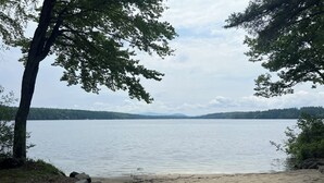 Vista de un lago con una playa arenosa, árboles y una costa lejana.