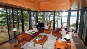 Un'ampia zona giorno con soffitto in legno, ampie finestre, una TV e un patio in legno.