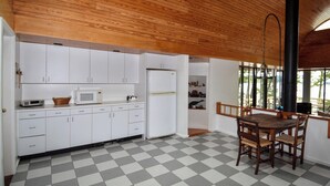 Cucina con mobili bianchi, forno a microonde e frigorifero. C'è un tavolo da pranzo con sedie e un pavimento a scacchi.