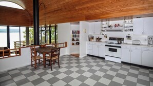 Una cucina con mobili bianchi, pavimento a scacchi e un'ampia finestra vista acqua.