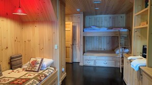 Interior acogedor de una cabaña con literas, una cama individual con colcha, paredes de madera y una pequeña kitchenette.