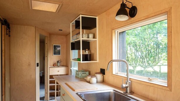 Cocina compacta con lavamanos integrado, armarios de madera y ventana con vistas a la vegetación.