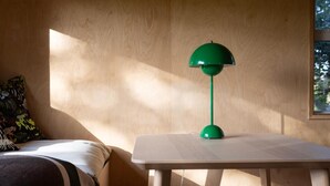 Una habitación con una cama, una mesita de noche con una lámpara verde y una ventana con luz natural.