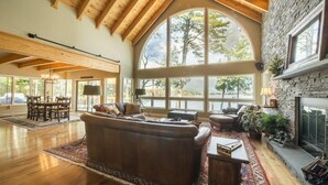 Un salón comedor amplio con techo alto, ventanas grandes, chimenea y pared de piedra.