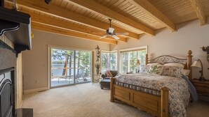 Un dormitorio con techo de madera, una cama, una mesita de noche, una lámpara y vistas al exterior.