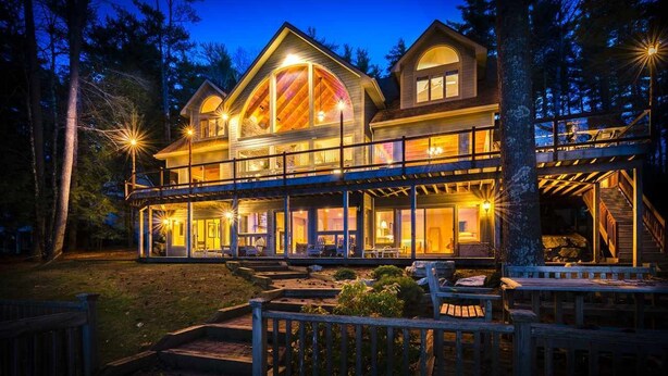 Una casa de madera grande de varios pisos, con un balcón, rodeada de árboles.