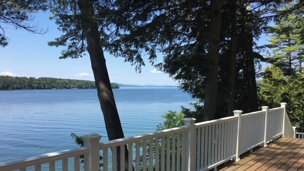 Une terrasse en bois avec une balustrade blanche donnant sur un lac.