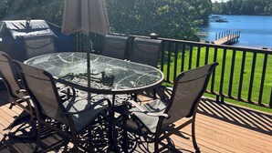 En terrass med ett glasbord och stolar, en grill och utsikt över en sjö.