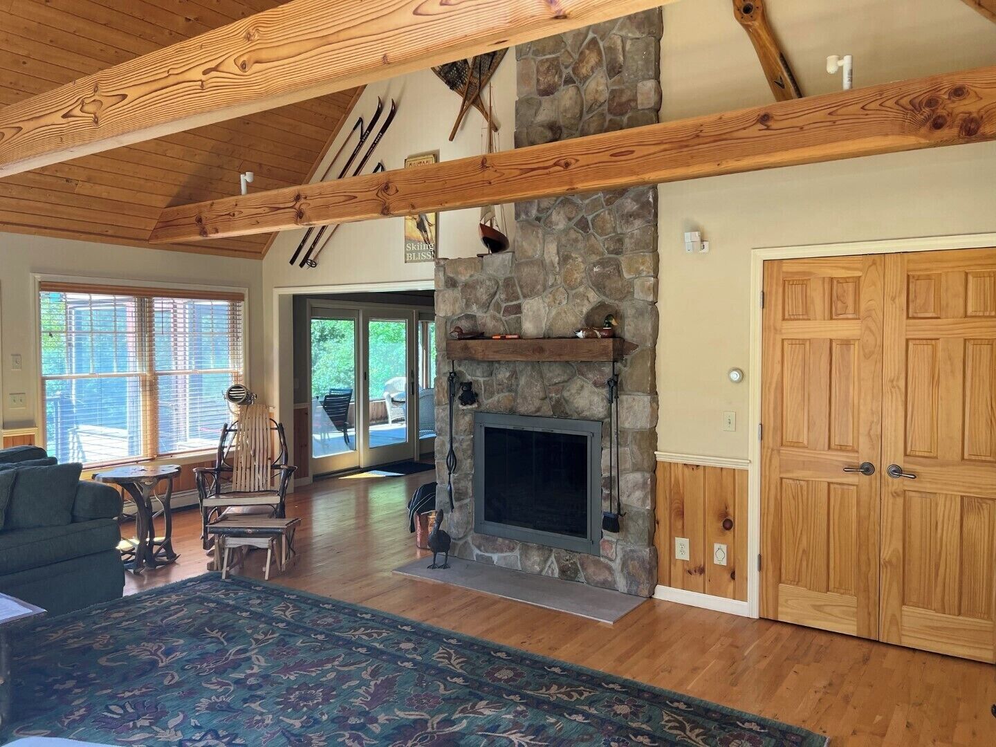 A spacious living room with a stone fireplace, wooden beams, and a large wooden door.