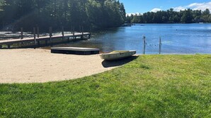 En brygga vid sjön med båtar, en gräsyta och en tät skog i bakgrunden.