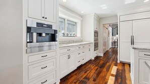 Cucina con mobili bianchi, cappa in acciaio inossidabile e pavimento in legno.
