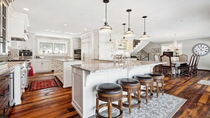 Un'ampia cucina con un'isola grande, illuminazione a sospensione e una zona pranzo con un orologio.