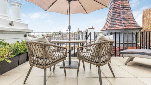 Une terrasse sur le toit, avec deux fauteuils en osier, une table et un grand parasol.