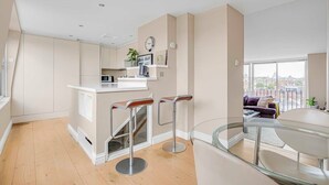 Une cuisine moderne dotée d’un îlot central, de tabourets de bar et d’un coin repas avec une table en verre.