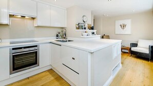 Une cuisine moderne avec des meubles blancs, un four encastré, un évier et un coin repas comprenant un canapé et une table.