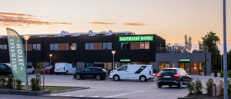 A modern hotel with a flat roof, multiple parking spaces, and a sign indicating 'EASY STAY HOTEL'.