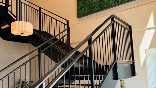 A modern staircase with black railings, a green wall art piece, and a potted plant. - Easy Stay Næstved (Næstved)