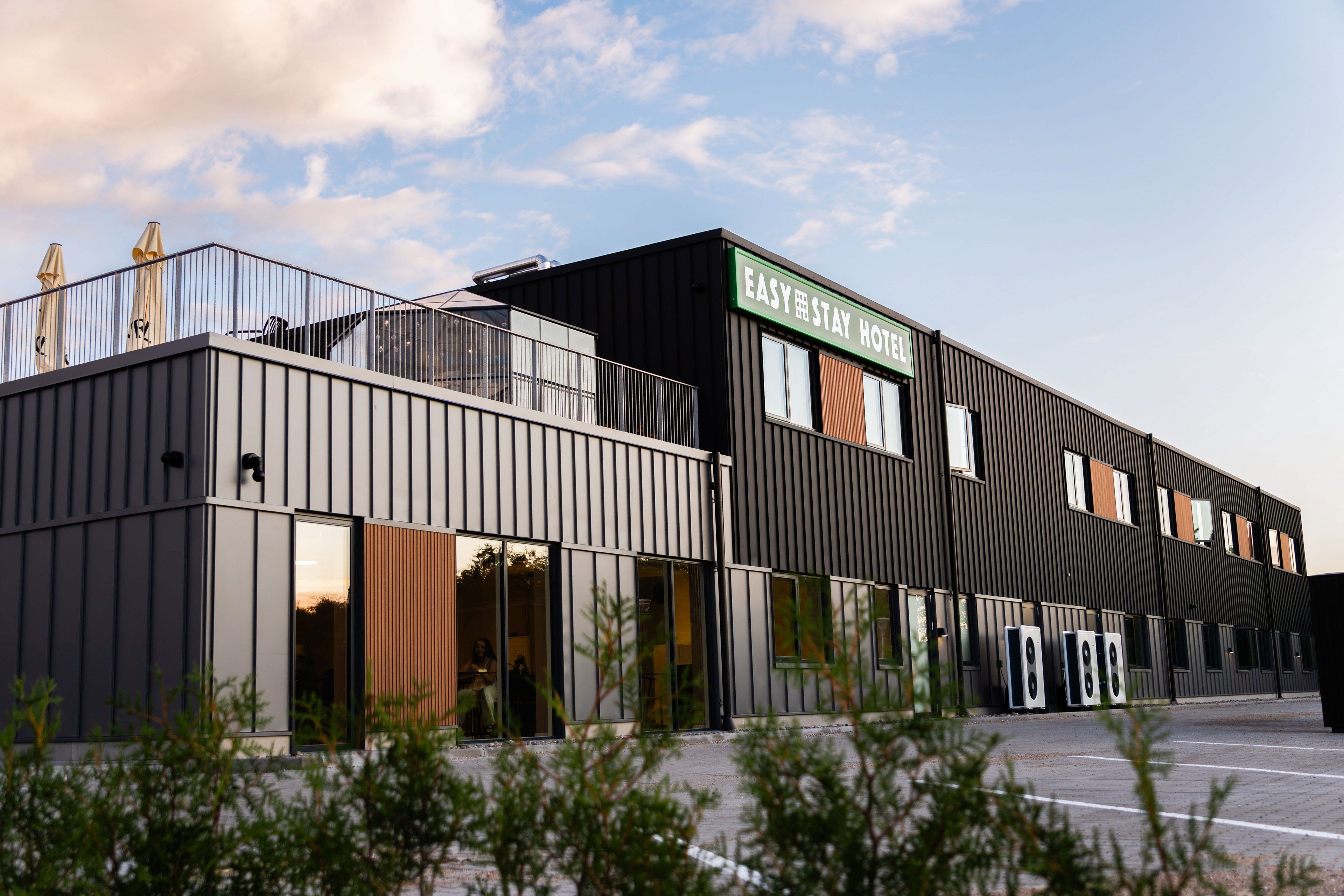 A modern hotel with a flat roof, large windows, and a sign that reads 'EASY STAY HOTEL'.