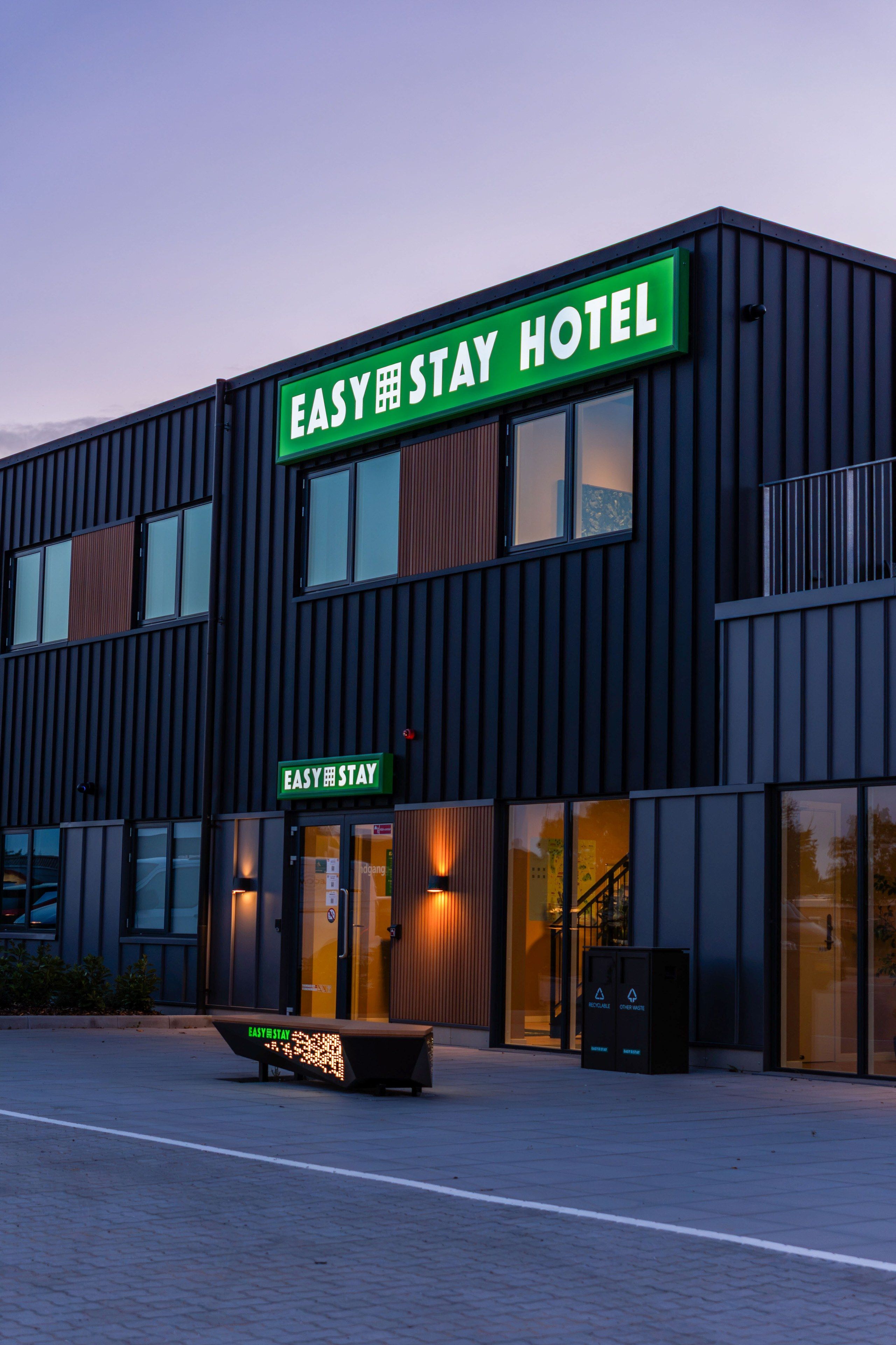 Um edifício moderno com uma placa indicando 'EASY STAY HOTEL' e um banco na frente.