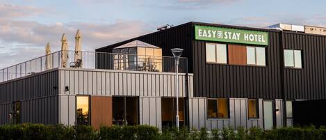 Un hotel moderno con techo plano, ventanas amplias y un letrero que dice 'EASY STAY HOTEL'.