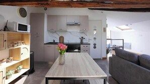 A modern kitchen with a dining area, wooden beams, a clock, and a vase with flowers. - Charming rooftop cocoon in Vizille (Vizille)