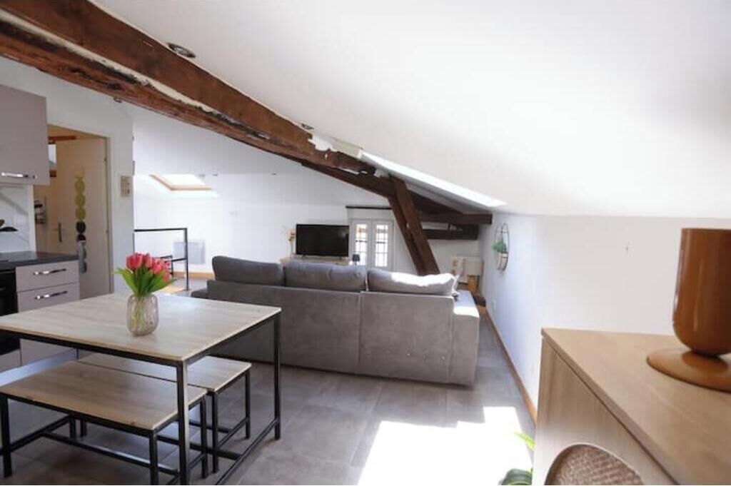 A loft-style room with a dining area, a sofa, and a television in the background.