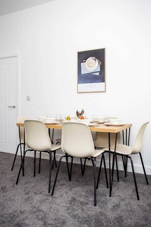 Un coin repas avec une table dressée pour quatre personnes, quatre chaises, un tableau encadré au mur et une porte sur la gauche.
