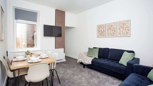 Ein modernes Wohnzimmer mit Essbereich, einem dunkelblauen Sofa und einem flachbildfernseher an der Wand.