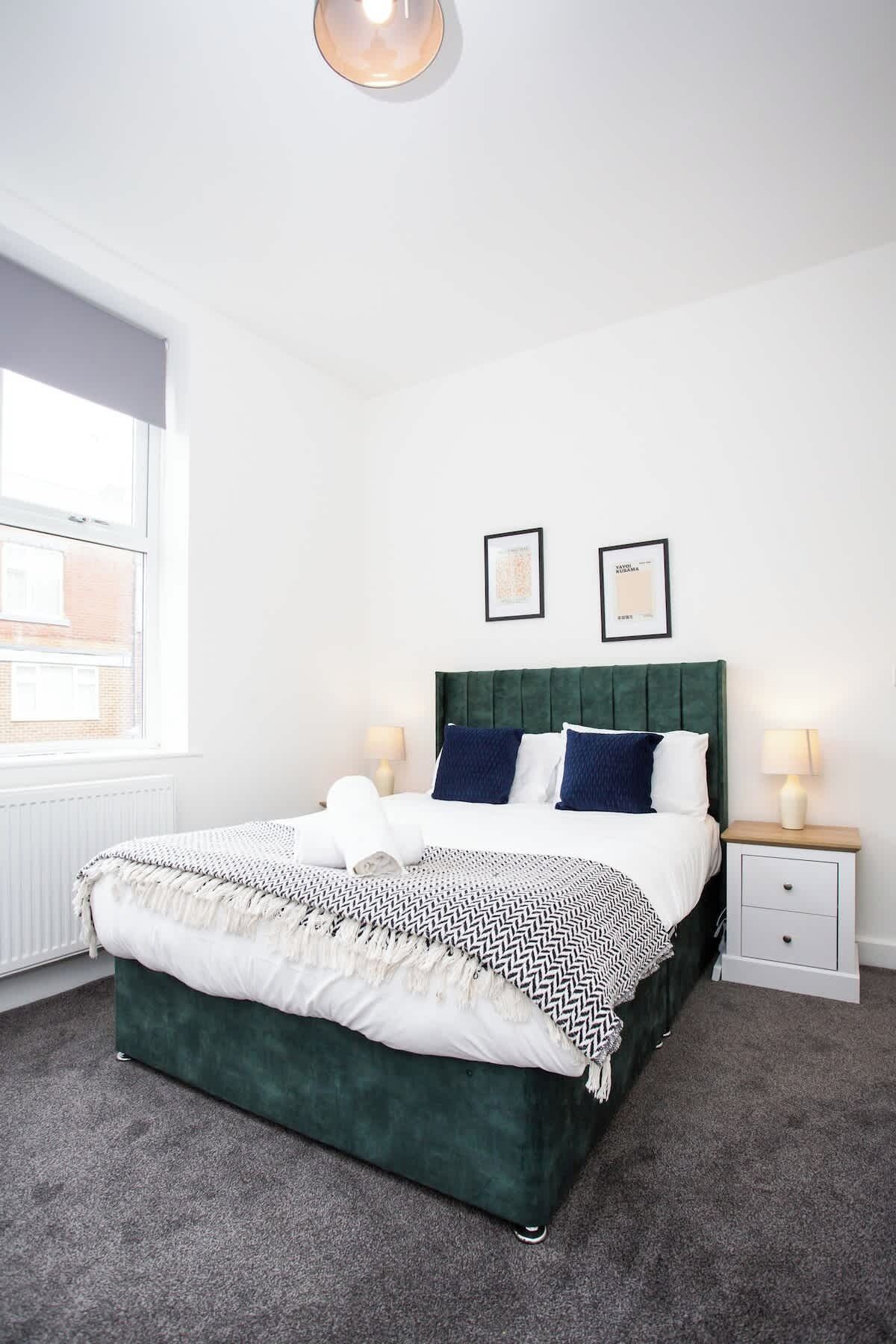 A bedroom with a bed, two bedside tables, a window, and two framed pictures on the wall.
