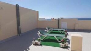 Eine Dachterrasse mit zwei grünen Liegestühlen, einem kleinen Tisch und Topfpflanzen.