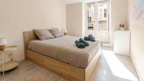A bedroom with a wooden bed, a nightstand, a lamp, and a view of the outside. - Cocon du Château - Elegant T3 in the historic heart of Vizille (Vizille)