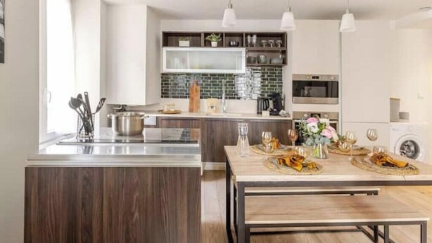 A modern kitchen with a central island, pendant lighting, and a dining area set for a meal. - Cocon du Château - Elegant T3 in the historic heart of Vizille (Vizille)