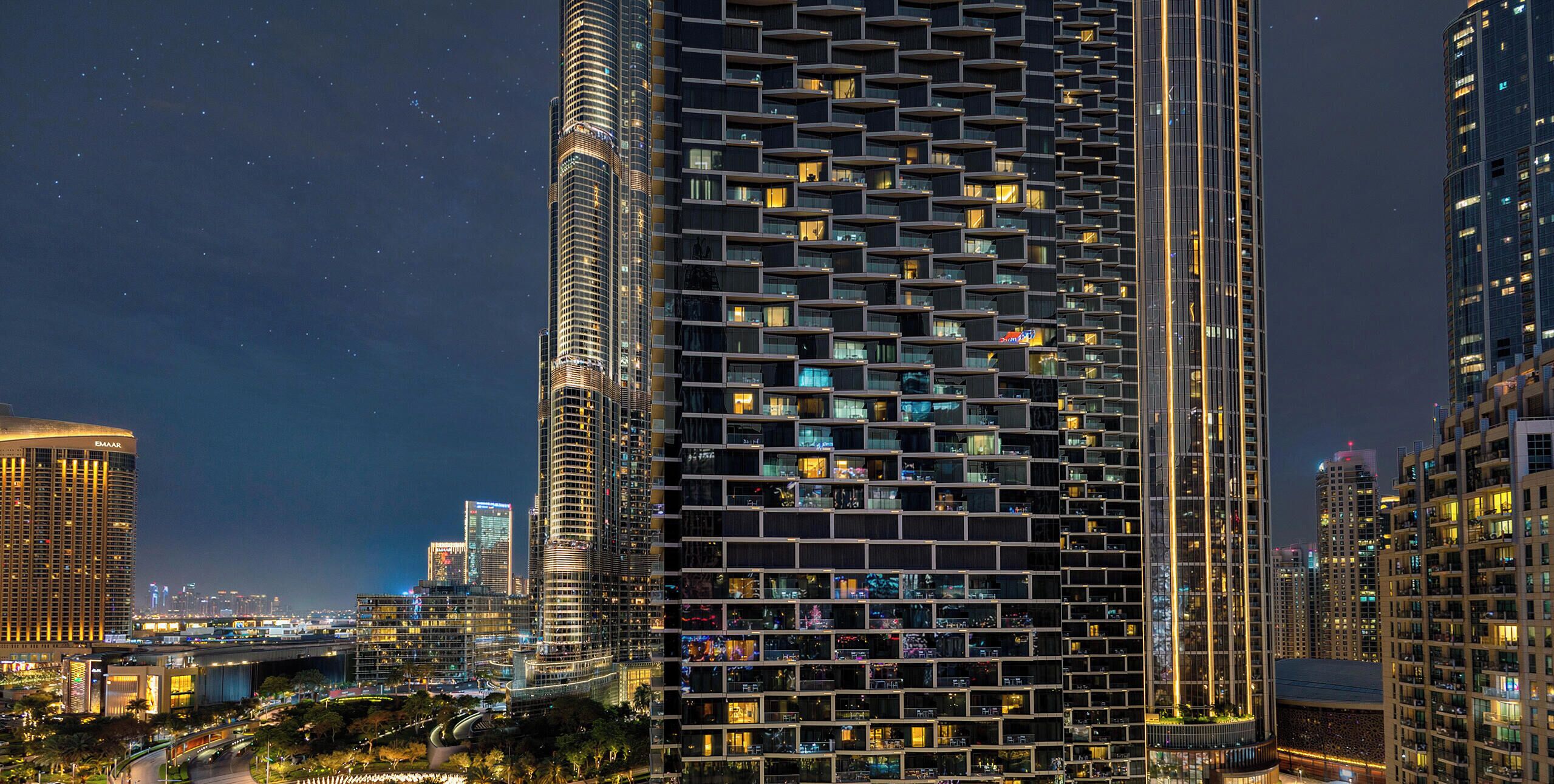 A high-rise building with a grid-like facade, multiple balconies, and illuminated windows at night.