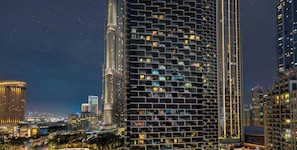 Een hoog gebouw met een gevel in rastervorm, meerdere balkons en verlichte ramen 's nachts.